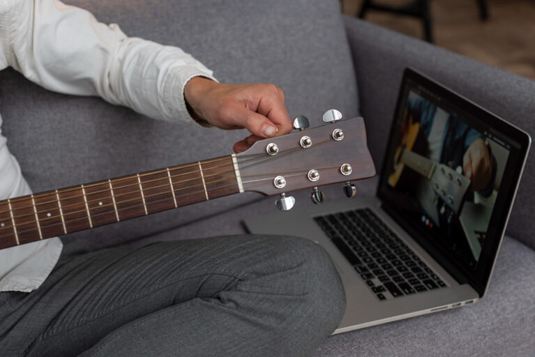 man-stemt-gitaar-met-laptop
